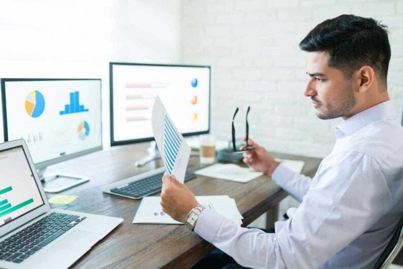 attractive young male sales professional analyzing chart while holding paper desk