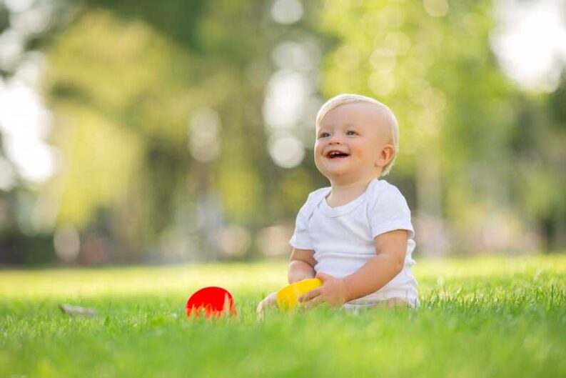 baby white bodysuit sitting green grass playing