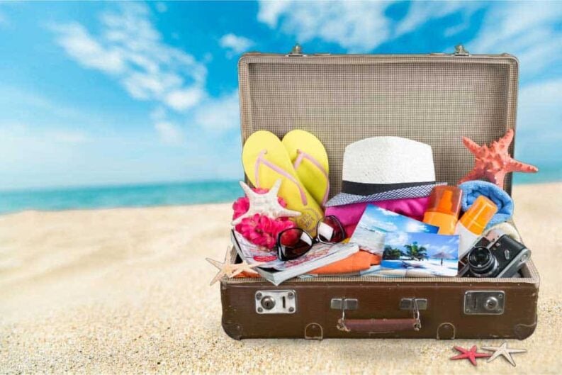 etro suitcase with travel objects tropical beach background