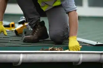 man worker is cleaning clogged roof gutter from dirt