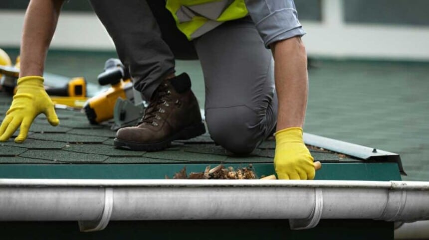 man worker is cleaning clogged roof gutter from dirt