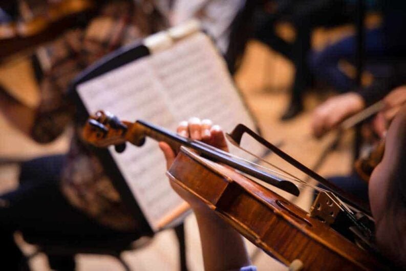 musician playing violin reading music sheet during classical music concert close up