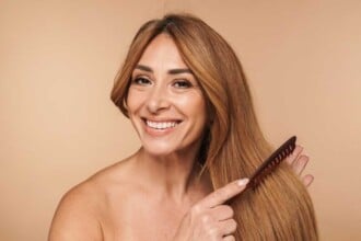 portrait shirtless adult woman brushing her hair smiling isolated beige