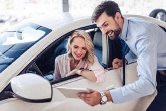 salesman talking with female client sitting car using digital tablet dealership salon