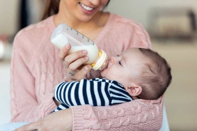 shot happy young mother feeding her baby son with feeding bottle home