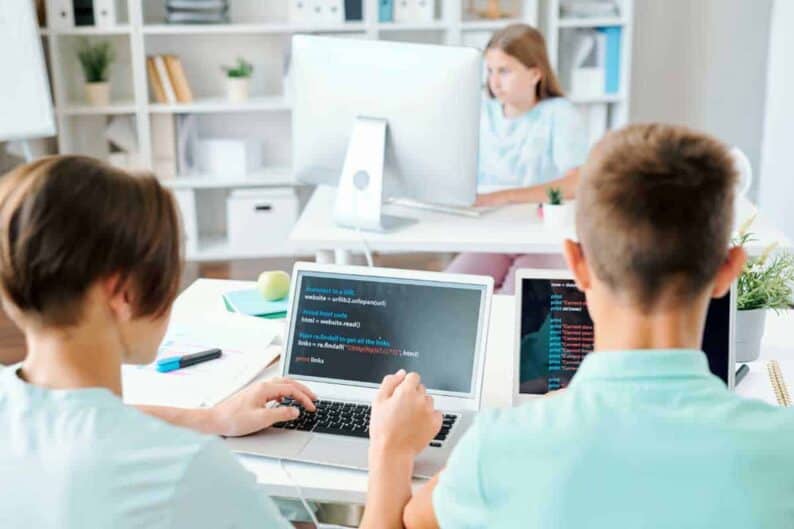 two schoolboys sitting by desk front laptops with schoolgirl networking by computer monitor 1