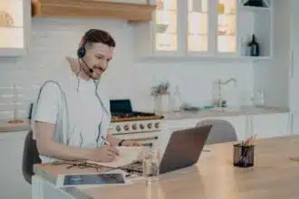 young bearded freelancer white tshirt sitting modern kitchen home using headset laptop while working remotely adult man studying online freelance distance education concept