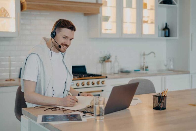 young bearded freelancer white tshirt sitting modern kitchen home using headset laptop while working remotely adult man studying online freelance distance education concept