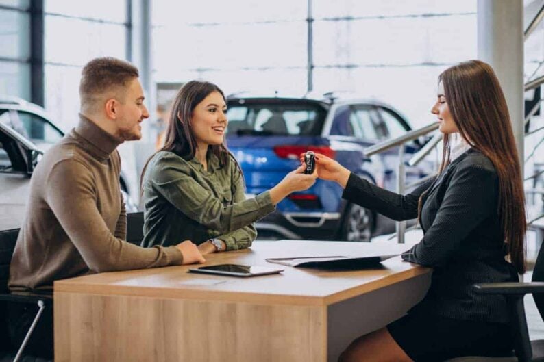 young couple talking sales person car showroom