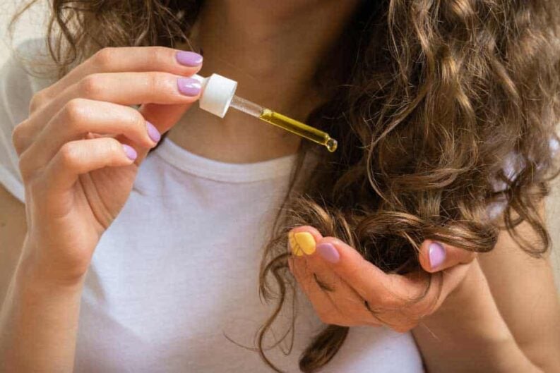 young girl caring curly hair tips with yellow oil