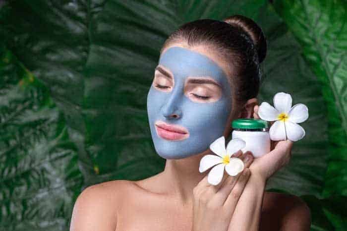 young lady with blue clay mask her face young woman holds plumeria flowers spa