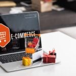 Toy gift boxes and credit card on laptop with e-commerce lettering on table