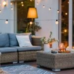 A residential patio with wicker furniture, textiles, and several types of warm lighting, including string lights and candles.