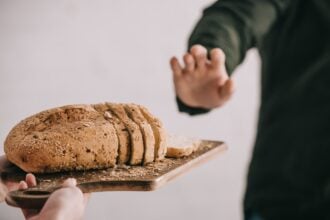 cropped view of woman holding cutting board with sliced bread near man with gluten intolerance